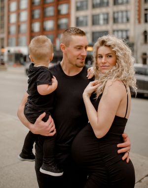 Family wearing coordinated black outfits poses together on urban street with brick buildings in background.