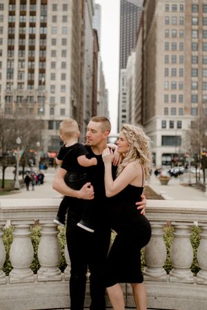 Family stands together on stone balcony with city skyscrapers in background.