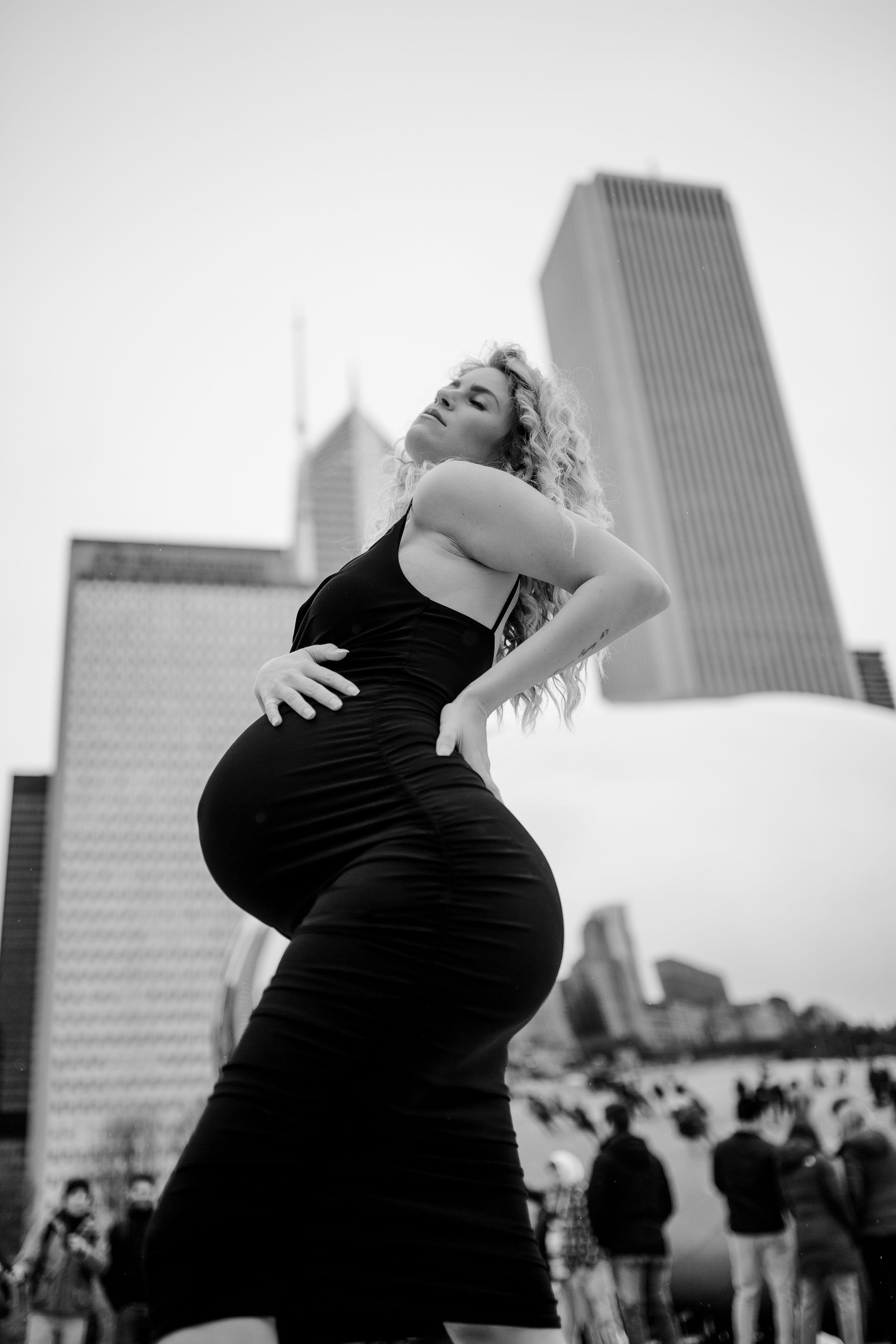 Dramatic black and white portrait of pregnant woman posing against urban skyline.