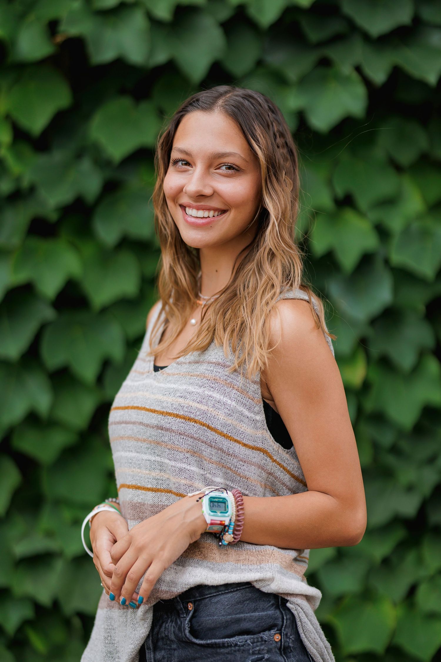 Casual summer style with striped tank top and denim against lush green ivy background.