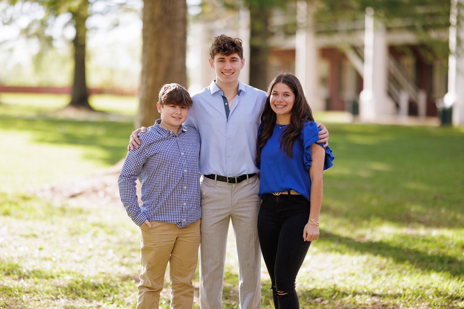 Three people pose together on a sunny day with trees and grass in the background.