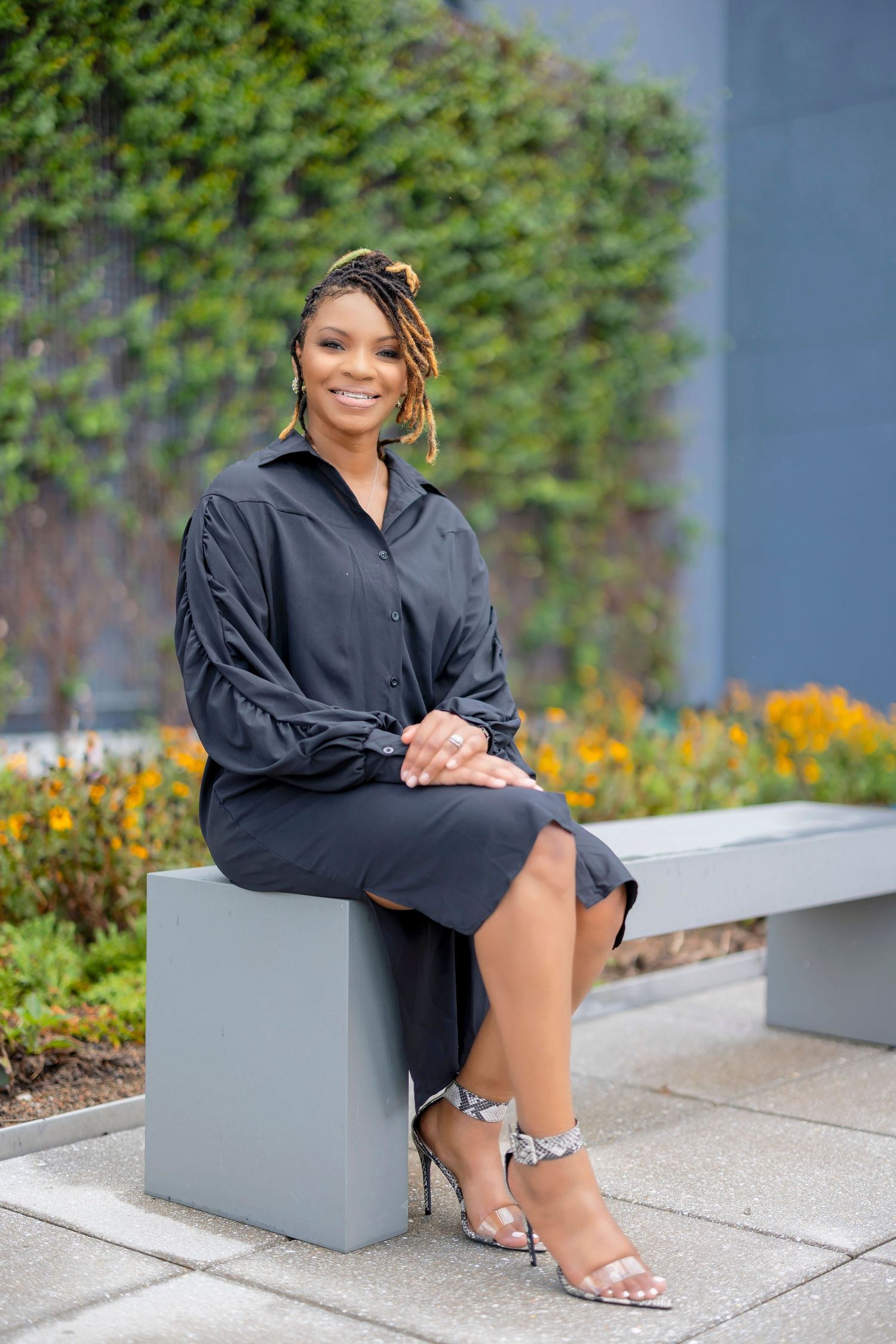 Stylish business attire featuring a black dress and heels while seated on modern concrete bench.