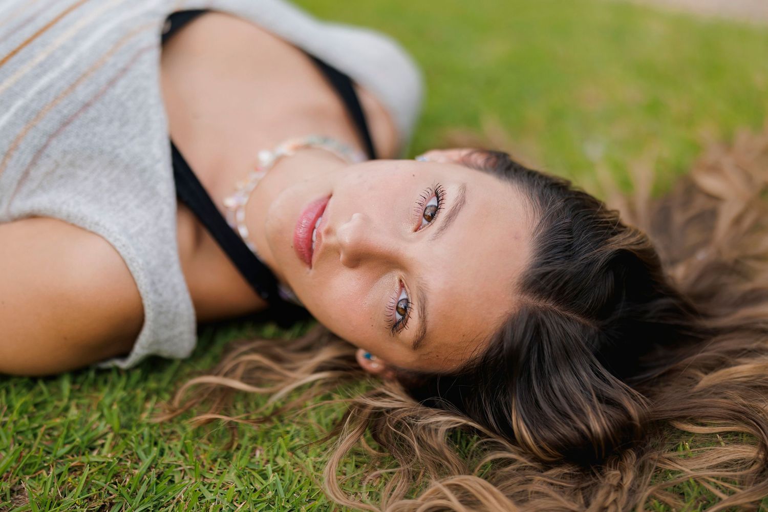 Artistic outdoor portrait lying on grass wearing casual grey tank top.