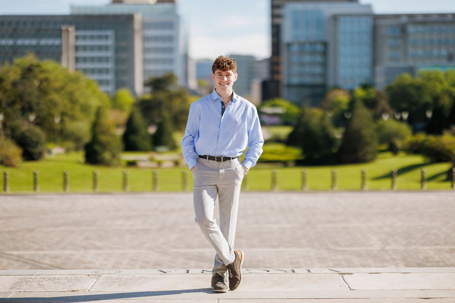 A person in business attire stands confidently on a plaza with modern buildings in the background.