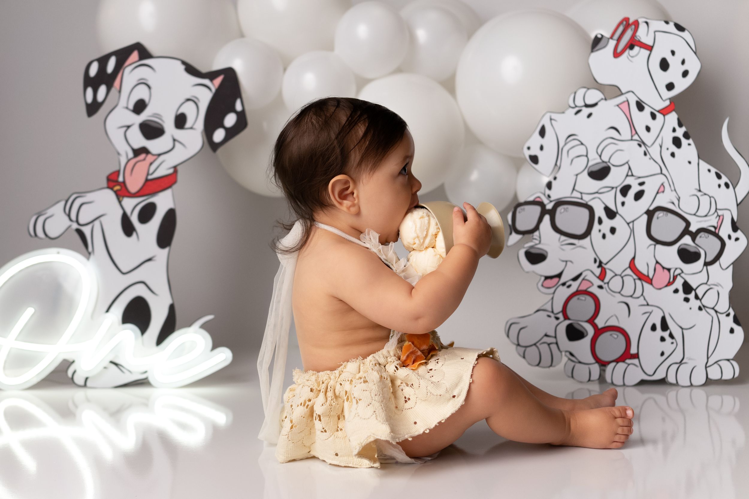 Studio photography first birthday setup featuring white balloons and cartoon dog decorations.