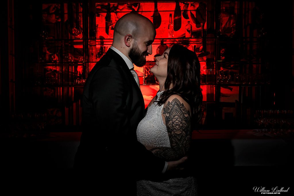 A dramatic wedding portrait with red backlighting creates a moody atmosphere.