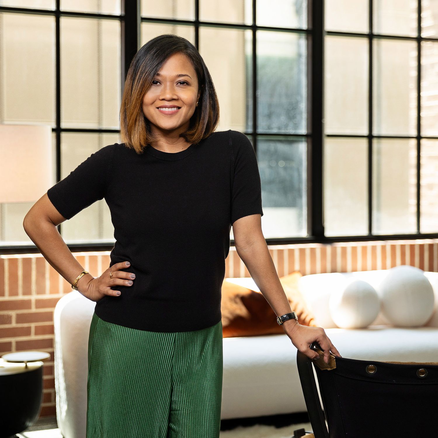 Person in black top and green skirt posing in modern industrial space with large windows.