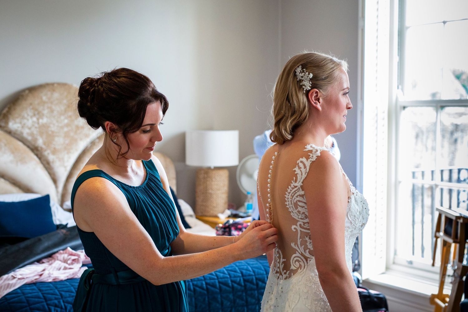 Close-up of detailed lace wedding dress being fastened near window.