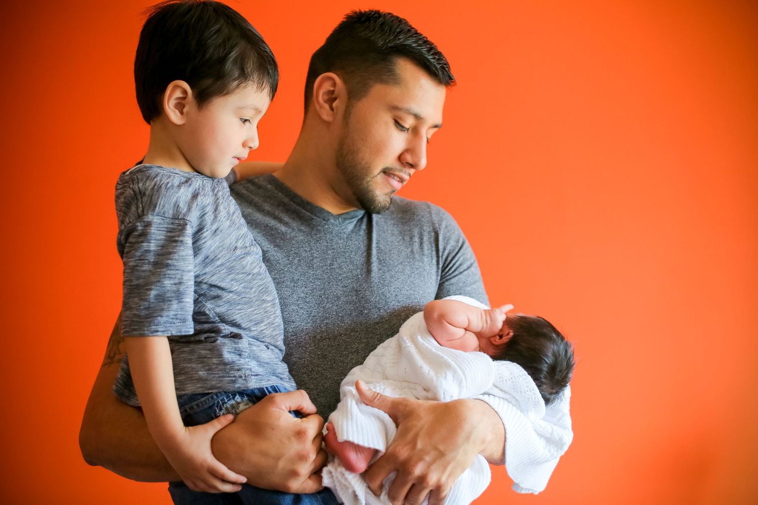 A newborn baby wrapped in white blankets being held against an orange background.