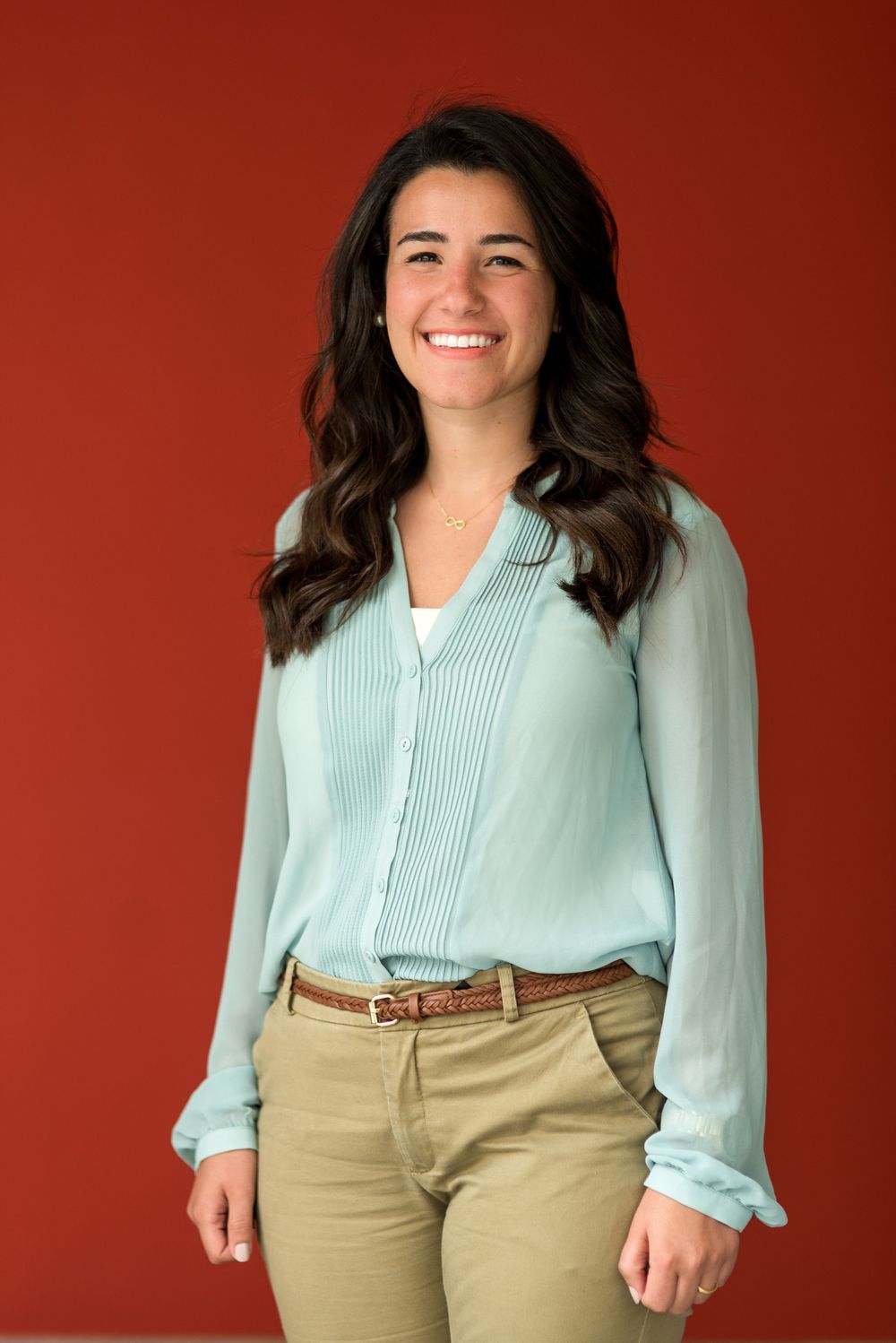Professional portrait of a person in mint green blouse and khaki pants against red background.