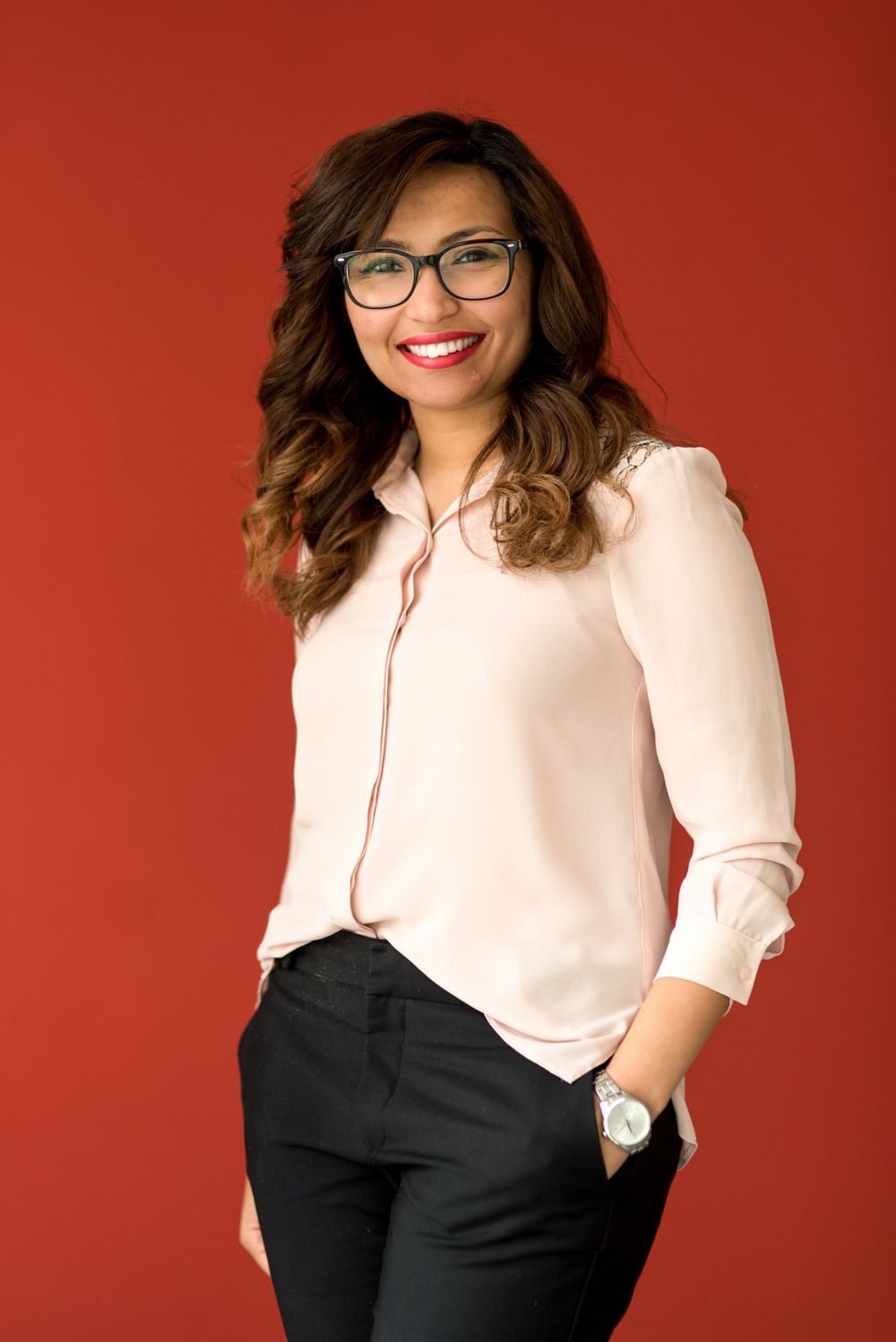 Professional portrait of a person wearing glasses and pink blouse against red background.