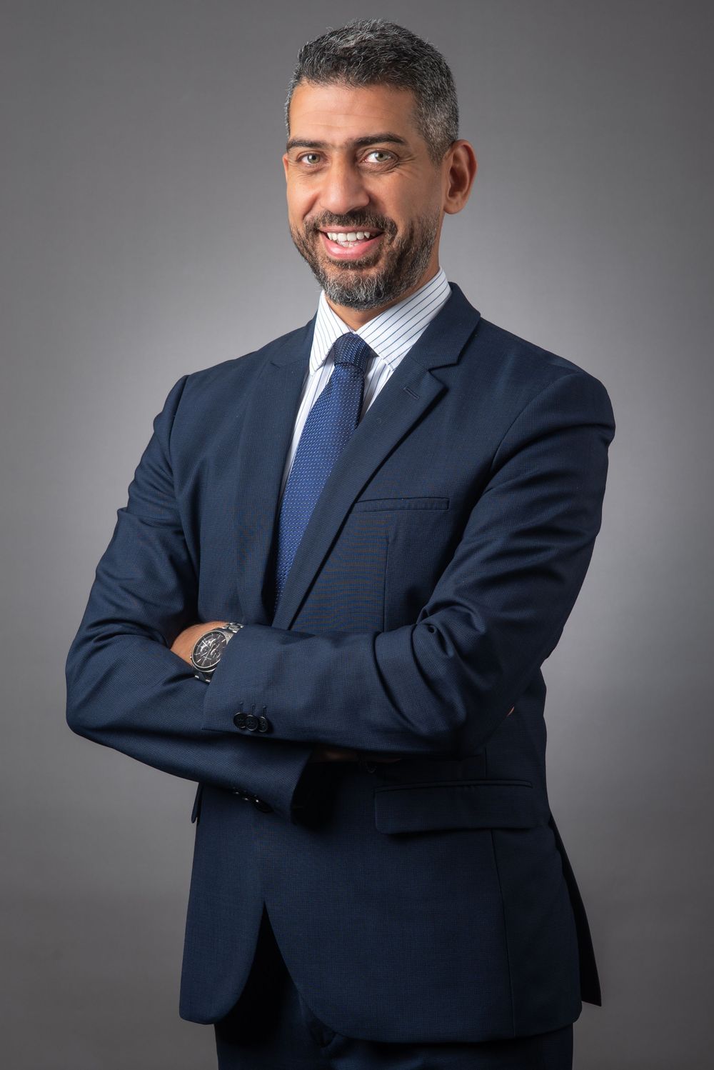 Professional studio portrait of a person in a dark suit with arms crossed.