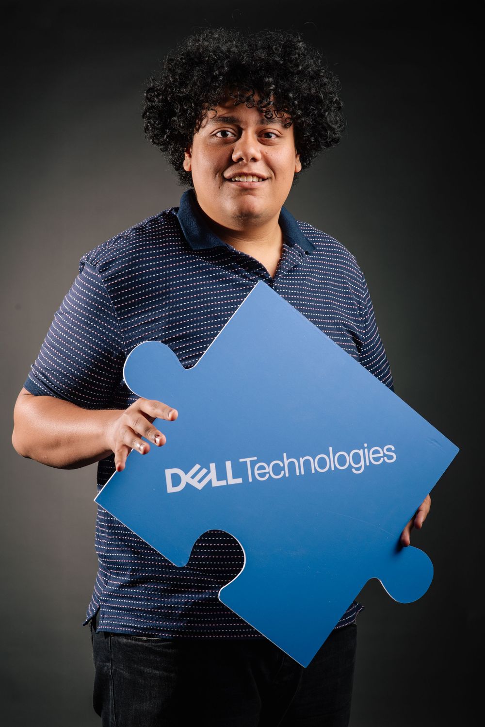 Team member holding large blue Dell Technologies puzzle piece against dark background.