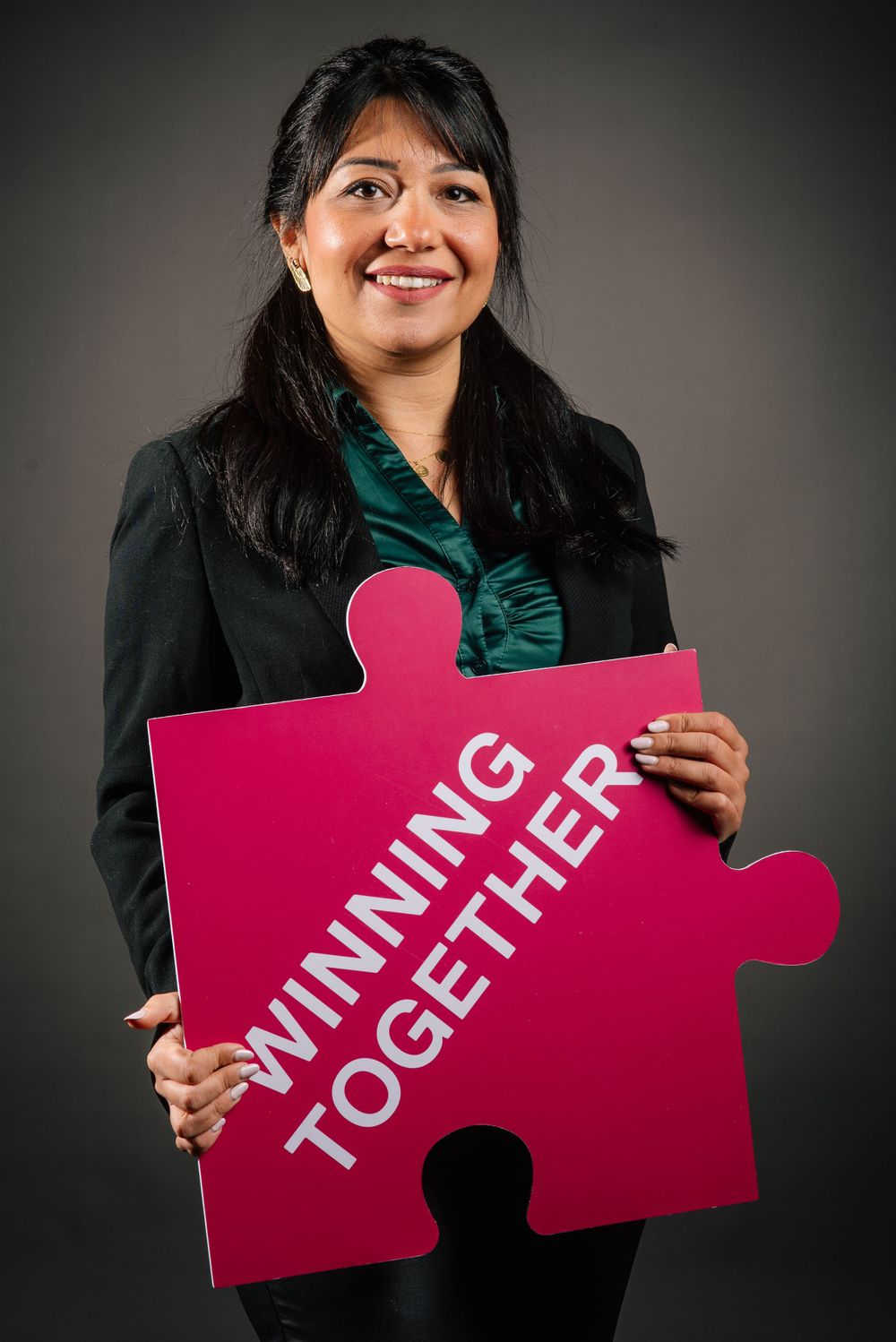 Professional in business attire holding pink Winning Together puzzle piece against dark background.