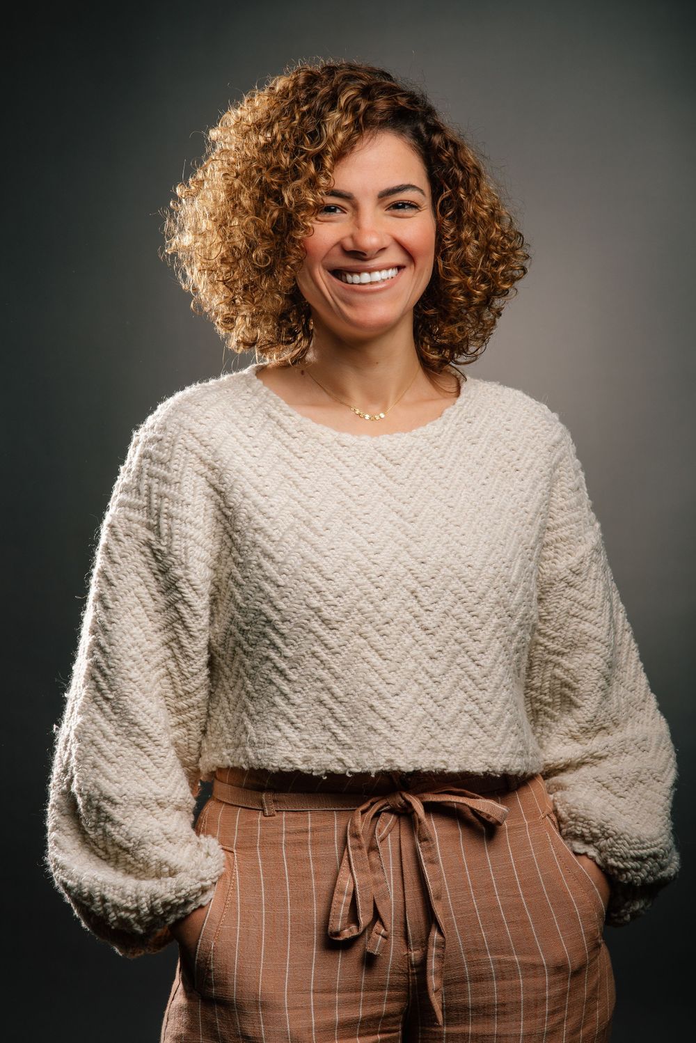 Stylish portrait of person in cream sweater and striped pants with natural curly hair.