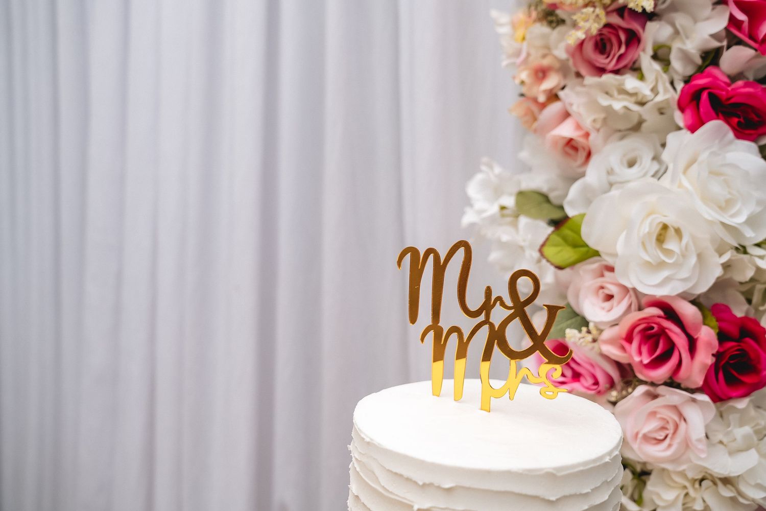 Wedding cake topper reading 'Mr & Mrs' surrounded by pink and white floral decorations.
