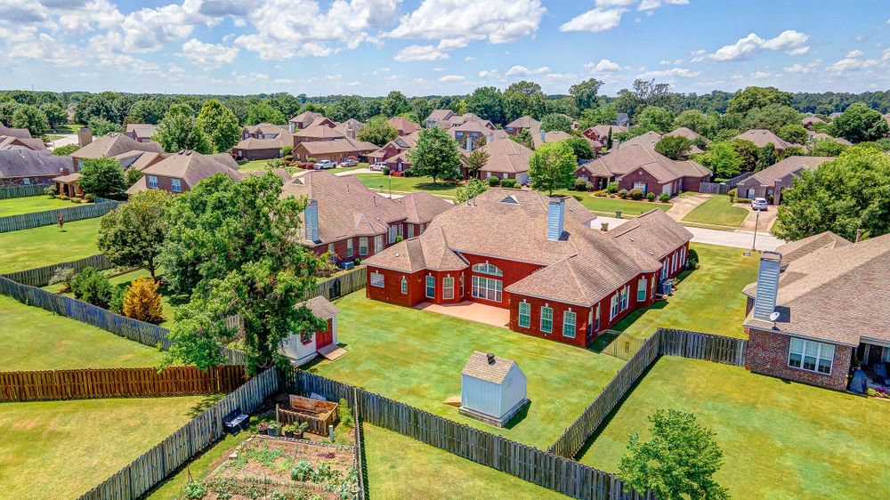Aerial view of suburban homes with red brick house and backyard pool in foreground.