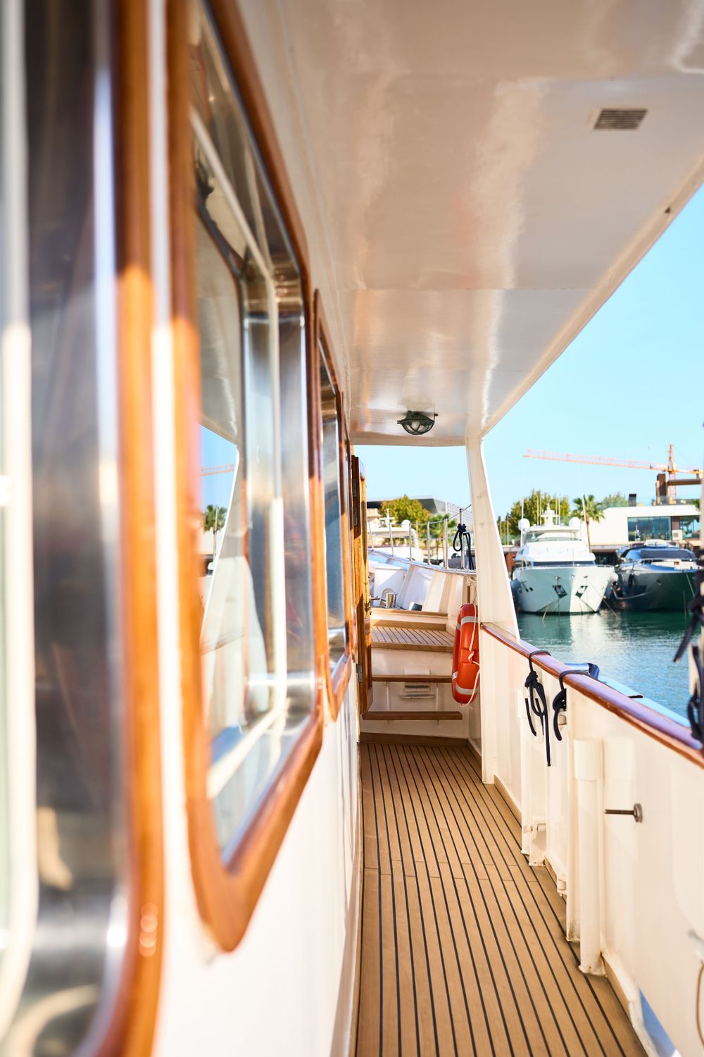 Wooden deck corridor of luxury yacht with marina view through windows.
