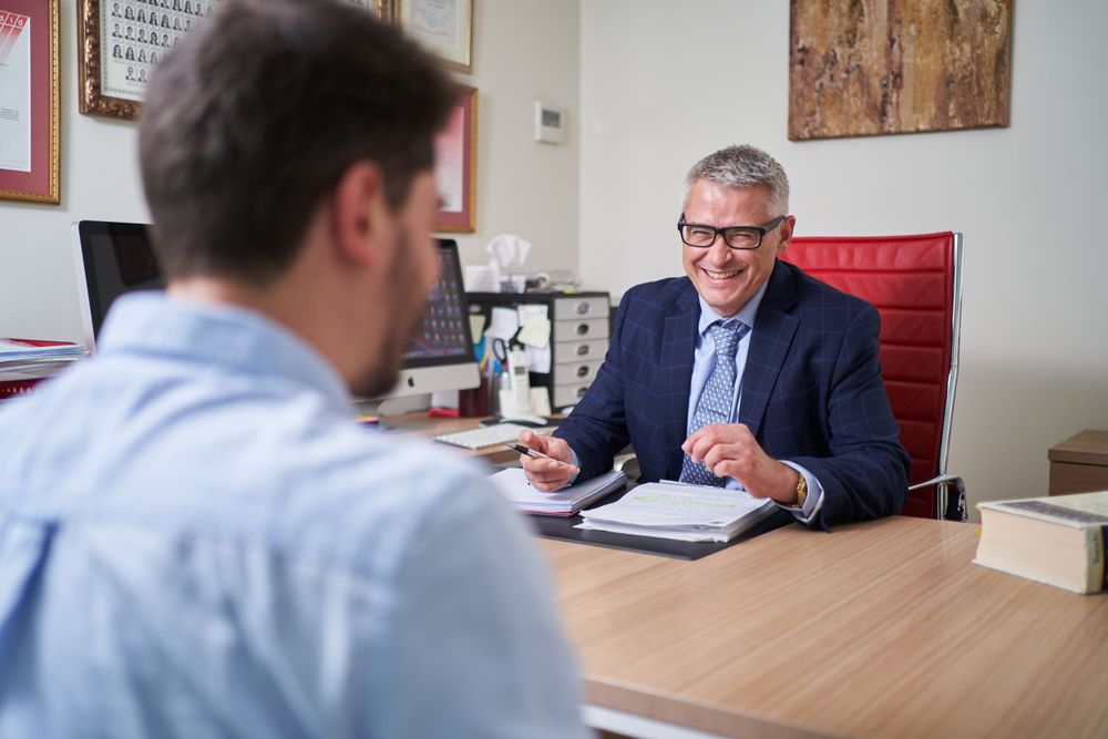 Business meeting between two people in a modern office with wood desk and artwork.