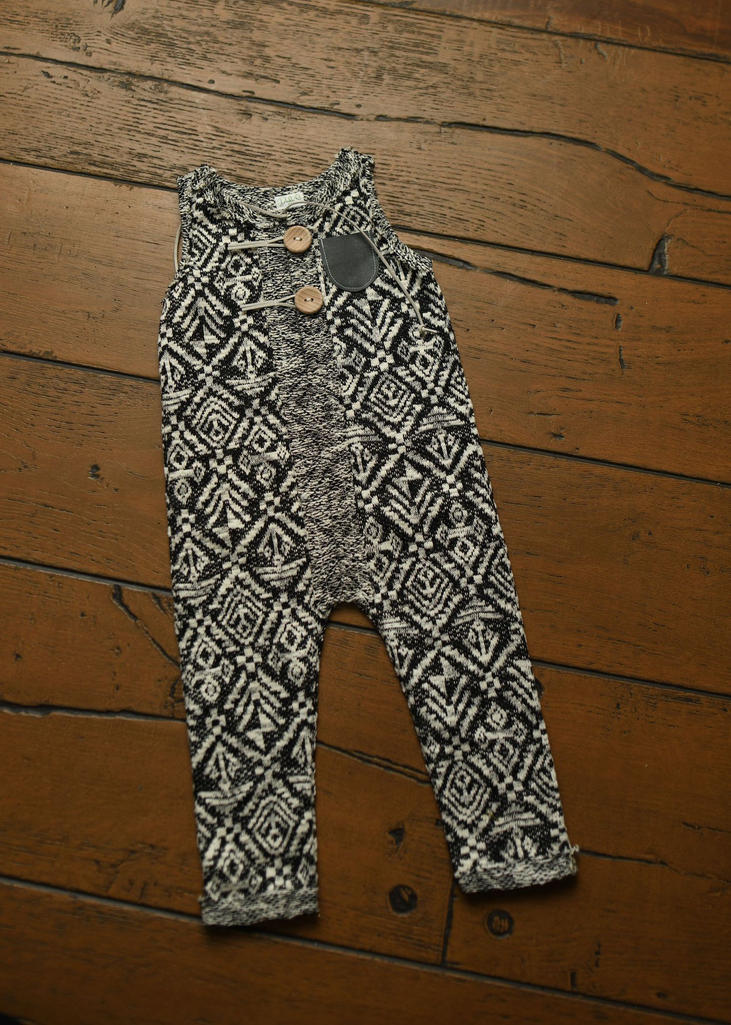 Black and white geometric patterned baby pants laid out on wooden flooring.