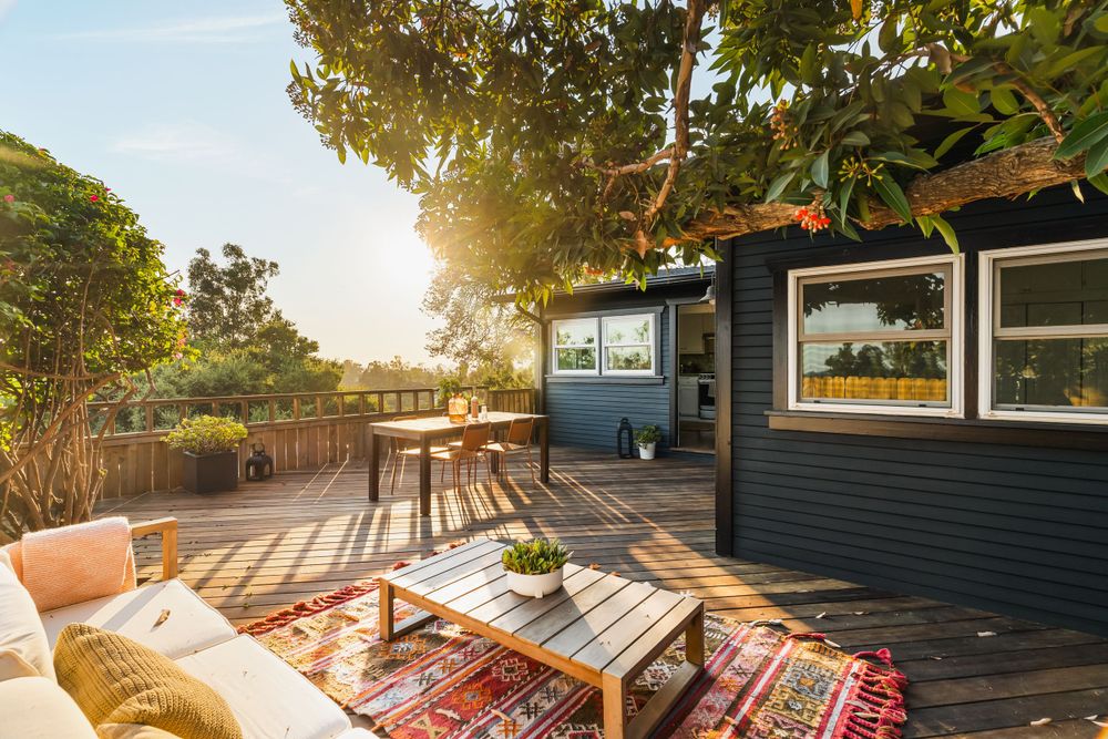Cozy outdoor deck with bohemian rugs and seating area against navy blue siding at sunset.