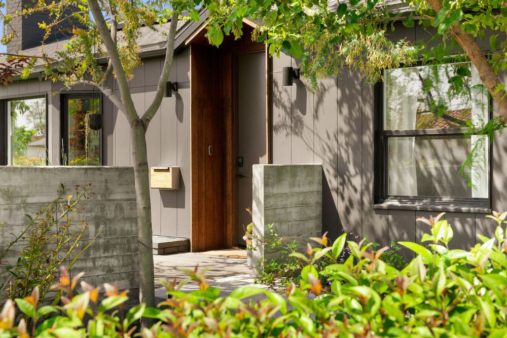 Modern house exterior with concrete and wood elements surrounded by lush greenery.