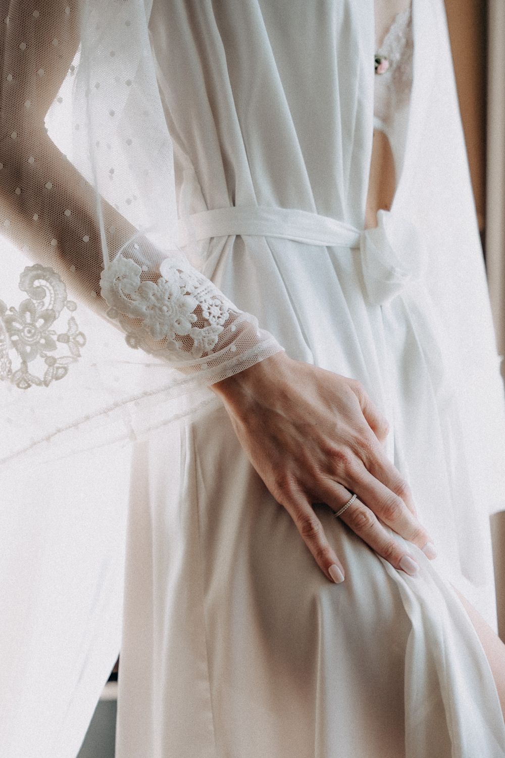 Close-up of white lace wedding dress sleeve detail with engagement ring.