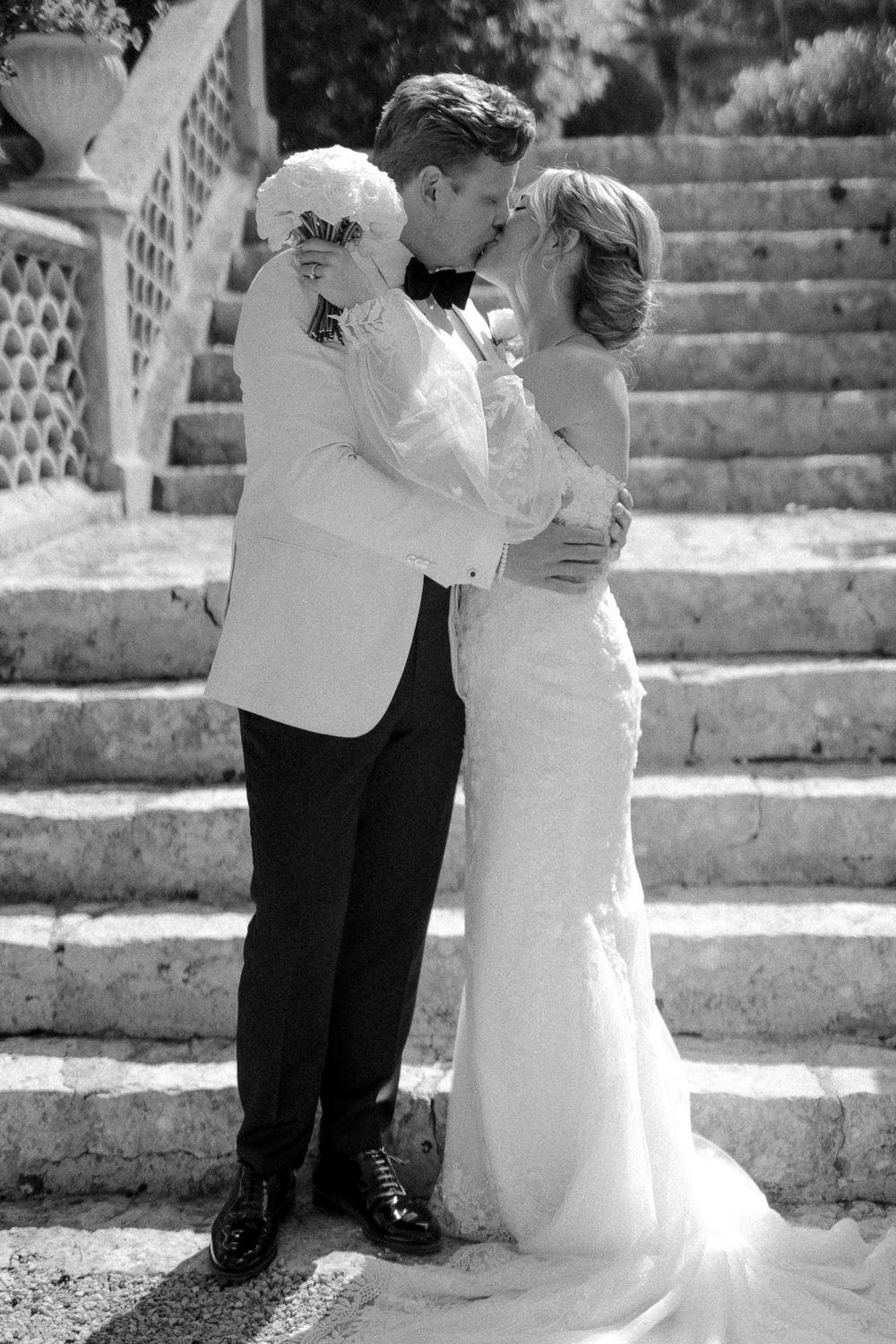 Black and white photo of newlyweds embracing on ornate stone staircase.