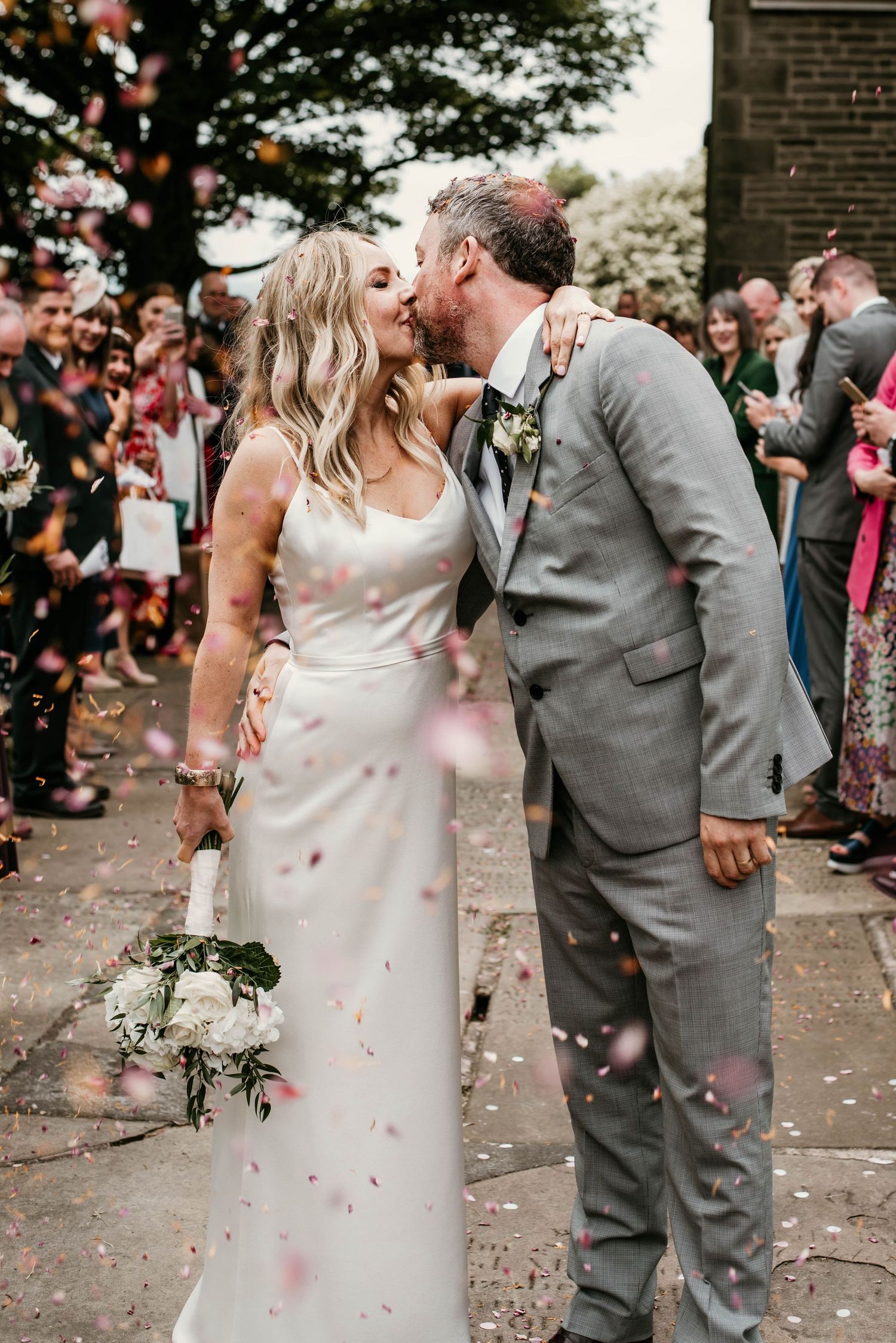 Bride and groom kiss during confetti shot in Marple church