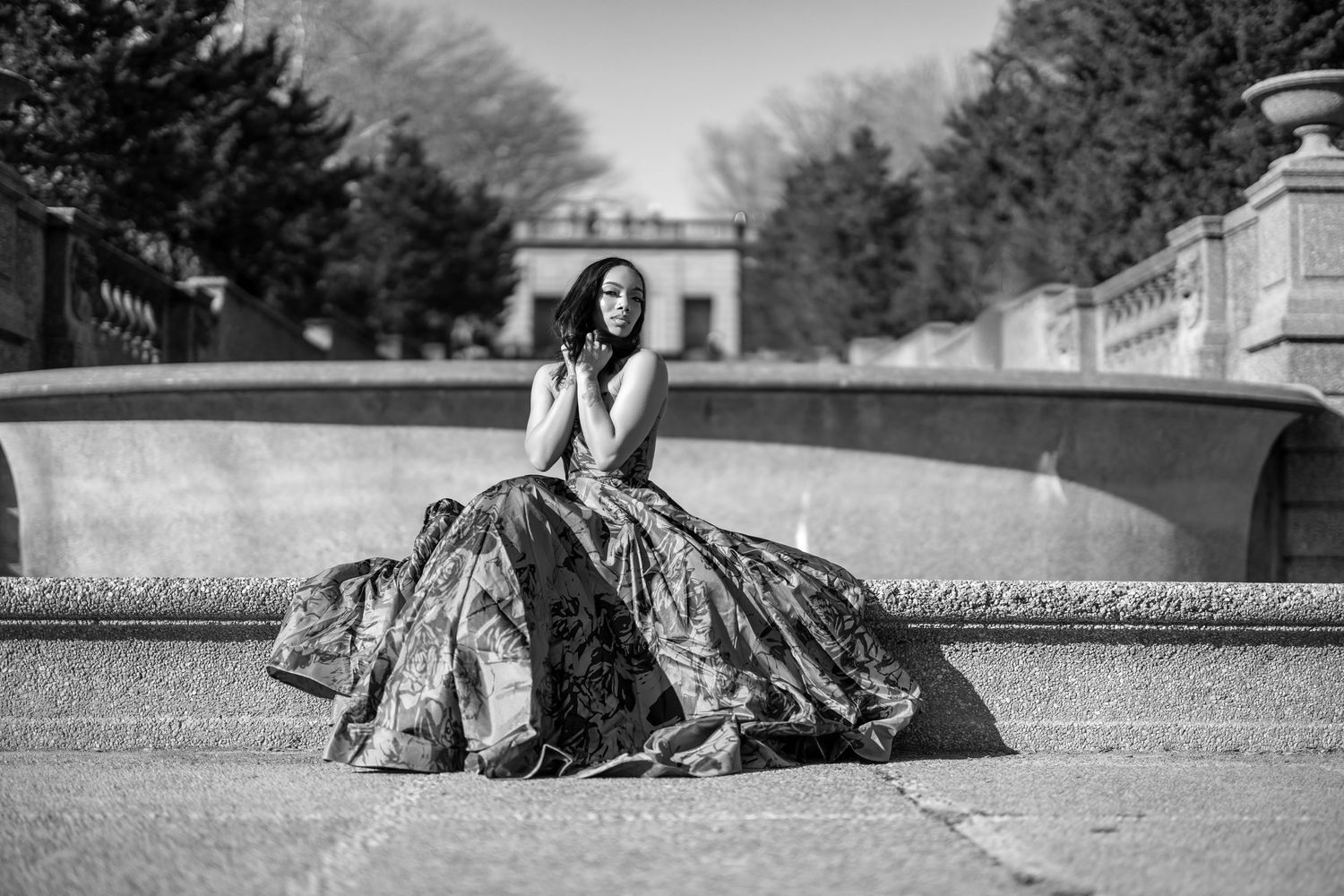 A dramatic black and white photo of someone in a voluminous gown seated on stone steps.