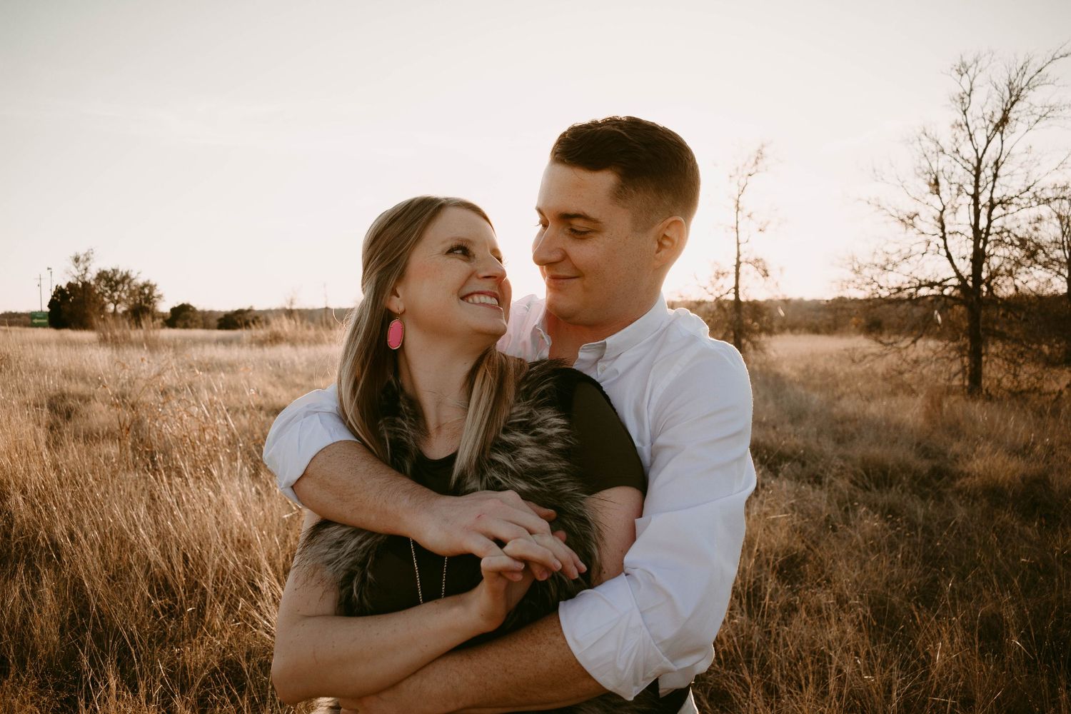 Couple sharing affectionate moment in rustic field during golden hour photoshoot.