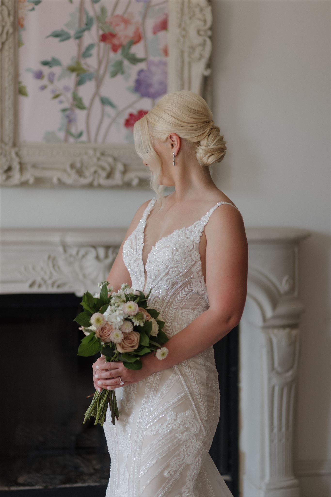 Side profile of wedding dress against floral artwork and ornate fireplace.