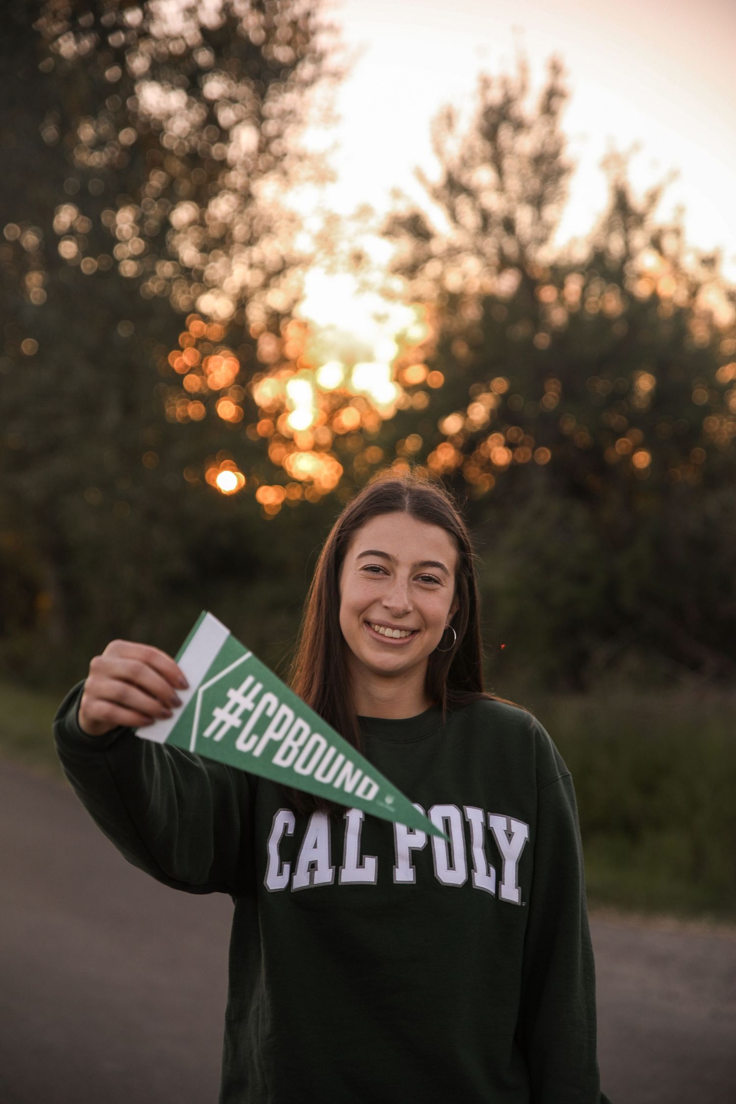 Student holding up Cal Poly acceptance letter during golden sunset in outdoor setting.