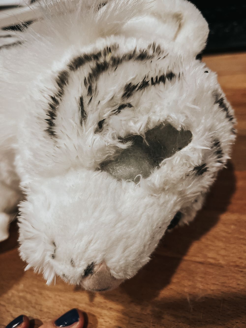 A Wild Republic stuffed white tiger toy laying down with a large hole where it's eye was.