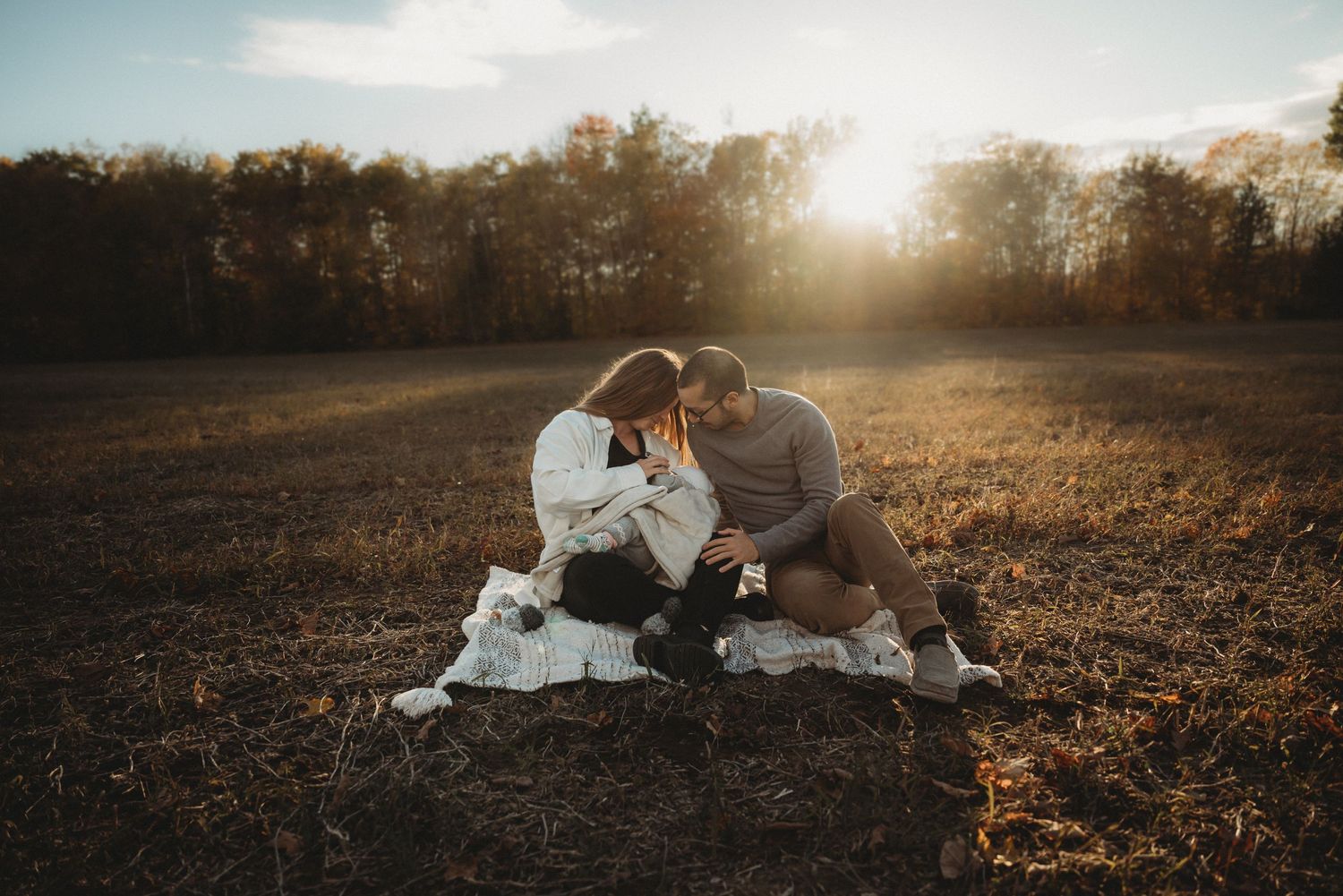 Couple sits on blanket in golden sunset field sharing intimate moment together.