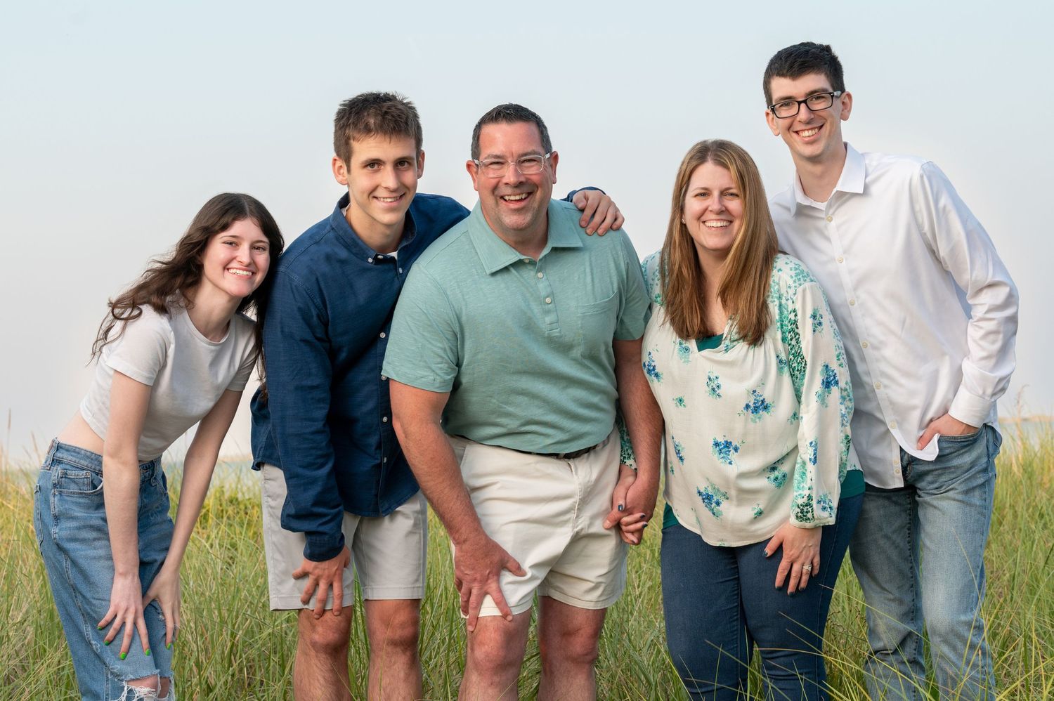A group poses together outdoors on a grassy hill in casual summer clothing.