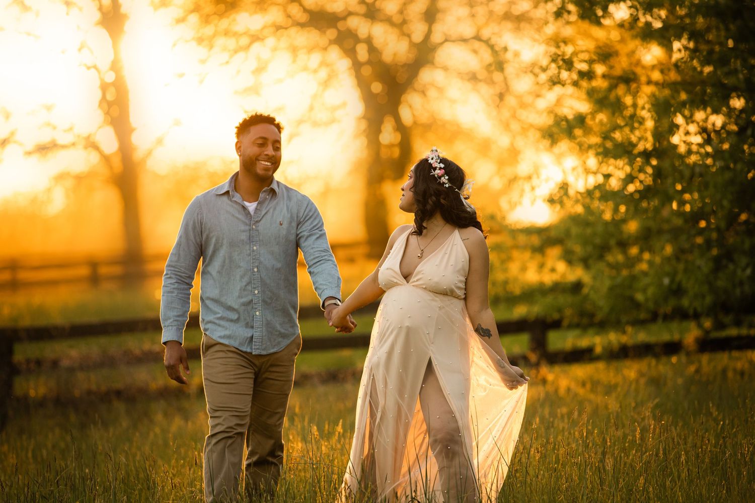Romantic sunset photo of an expecting couple walking through a golden field.