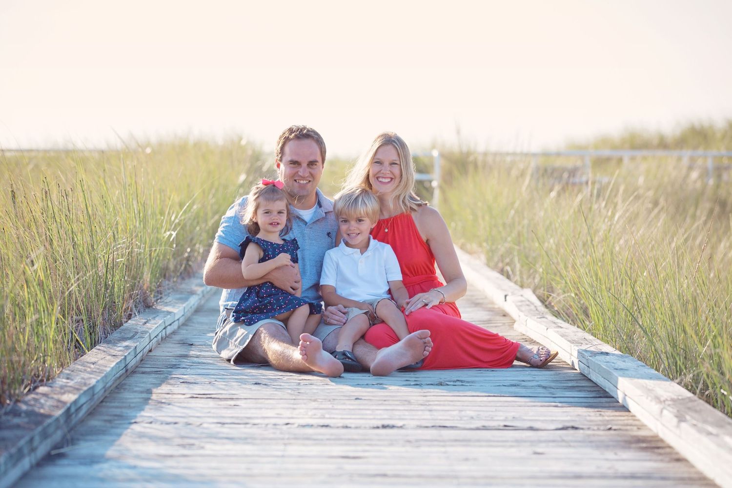 Family relaxing together on a wooden boardwalk surrounded by coastal marsh grass.