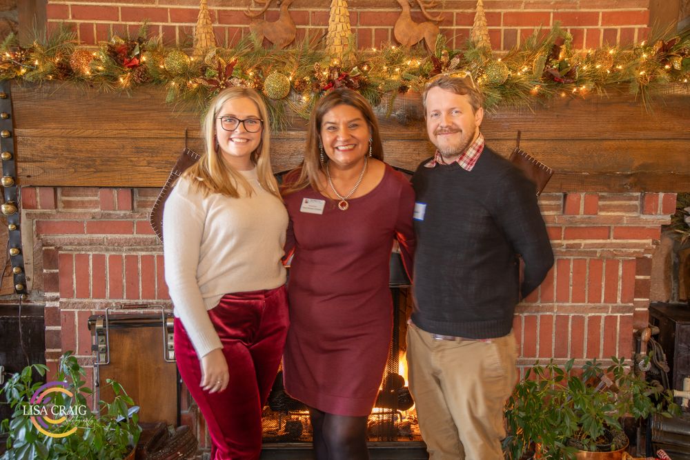 Three people posing for holiday photo by decorated brick fireplace with festive garland.