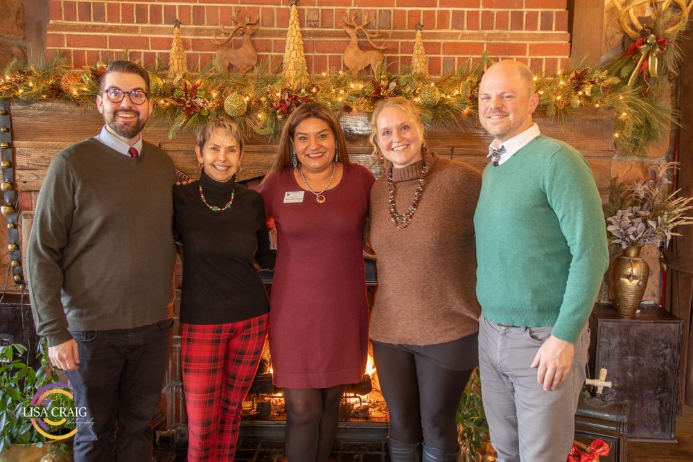 Five people gathered for holiday photo in front of decorated brick fireplace.