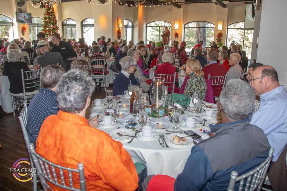 Guests gathered at round tables in an elegant dining room with large arched windows.