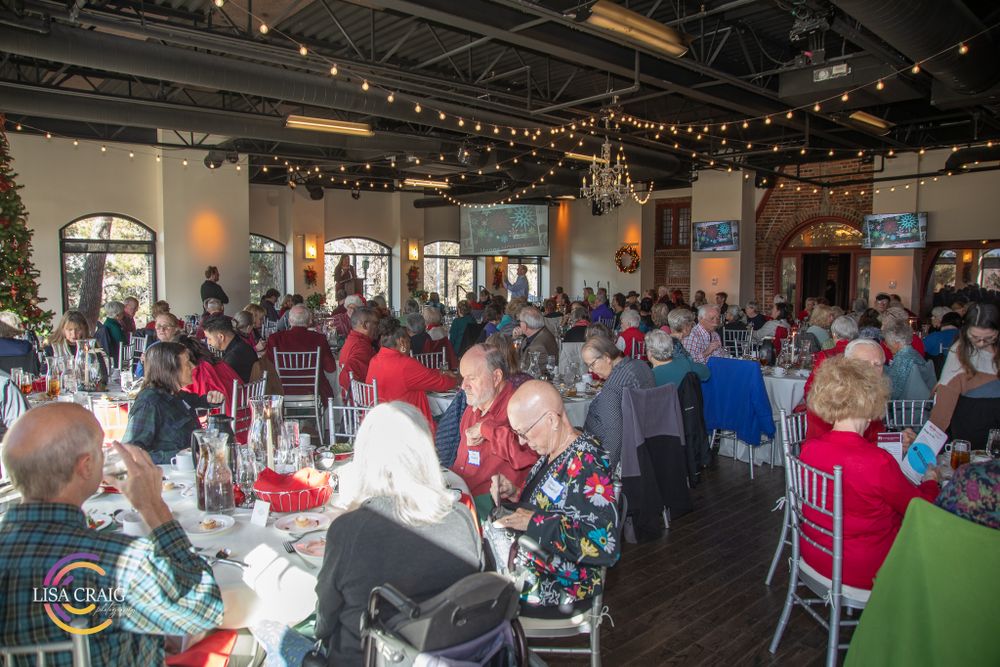 A festive dining room with string lights and arched windows filled with guests at round tables.
