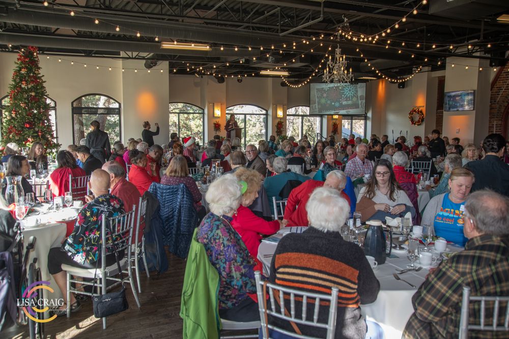 A crowded banquet hall with diners seated at decorated round tables under string lights.