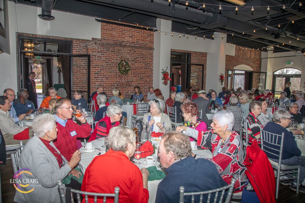 Crowded dining room filled with guests in red and holiday attire at round tables.