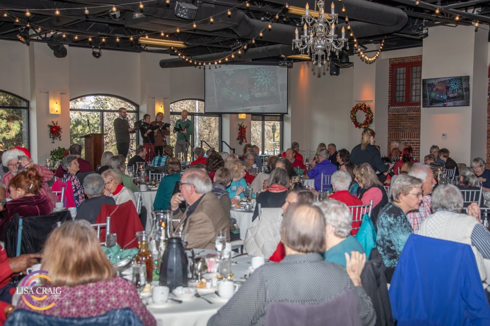 Banquet hall decorated for holidays with string lights and tables of guests.