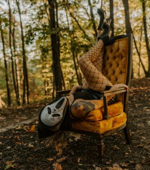 Vintage velvet chair with fishnet stockings and pumpkins in moody autumn forest setting.