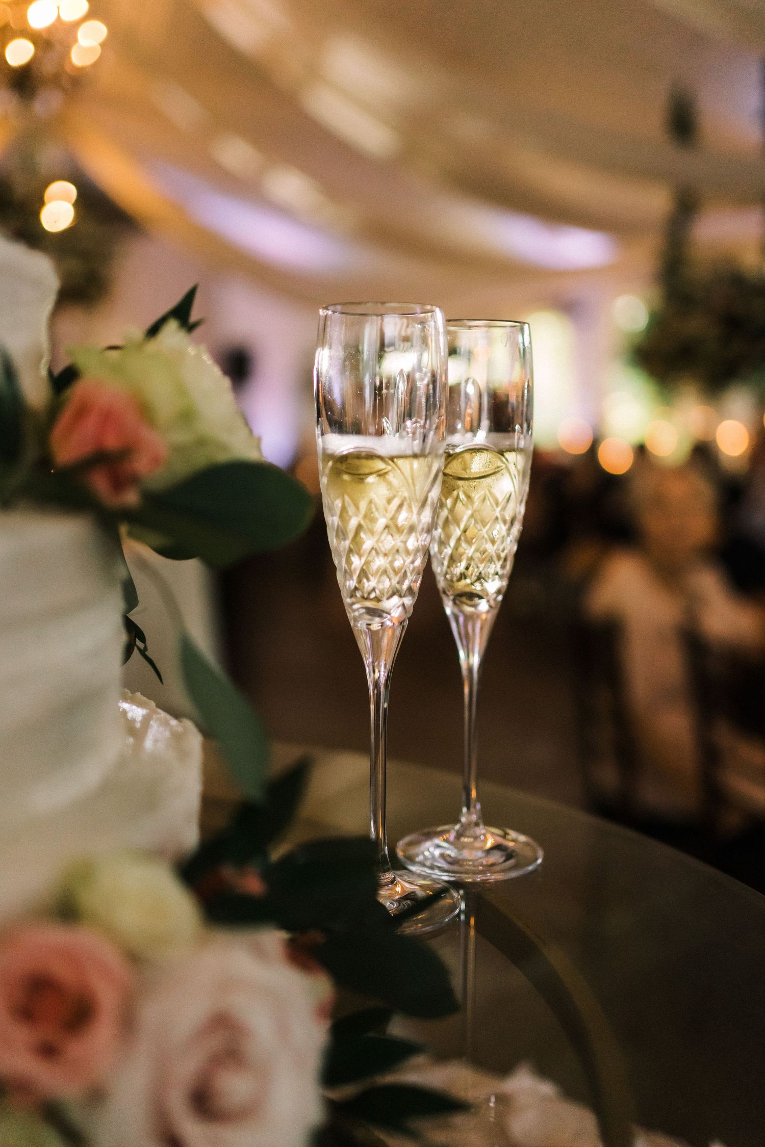 Elegant champagne flutes with sparkling wine sit among floral decorations at a wedding reception.