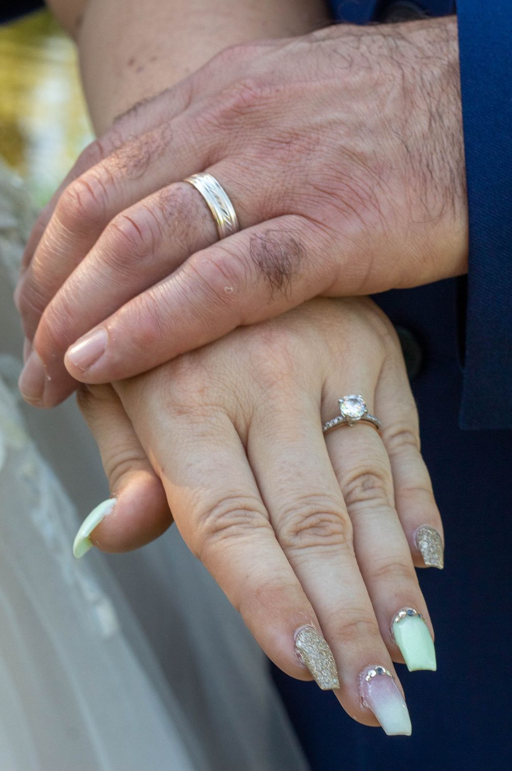 Close-up of newlyweds' hands showing wedding rings and decorated nails.