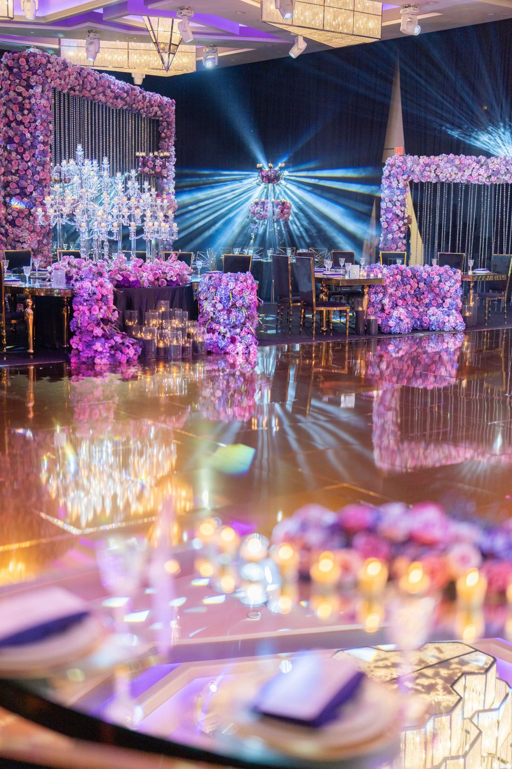 Luxurious wedding reception venue with purple floral arches and dramatic lighting effects.