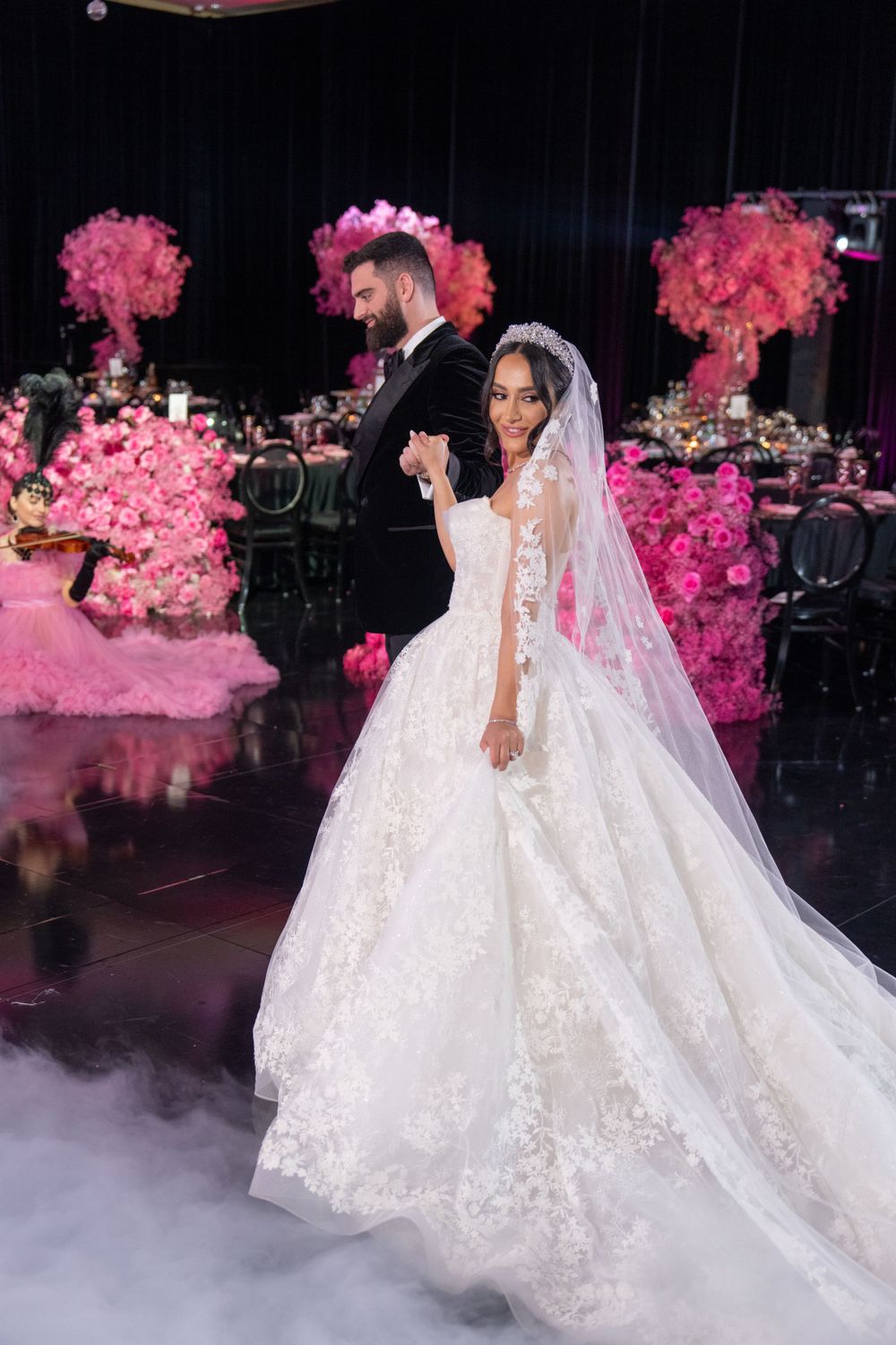Wedding couple dancing on misty floor surrounded by pink floral arrangements.